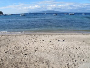 Una playa con huellas y un neumático en la arena, barcos en el agua y una montaña al fondo.