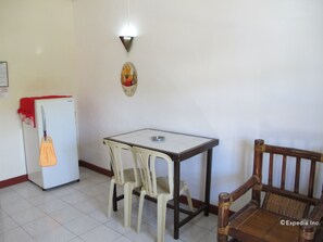 A small dining area with a white refrigerator, a table, two chairs, and a wooden chair. - Seashore Beach Resort (Puerto Galera)