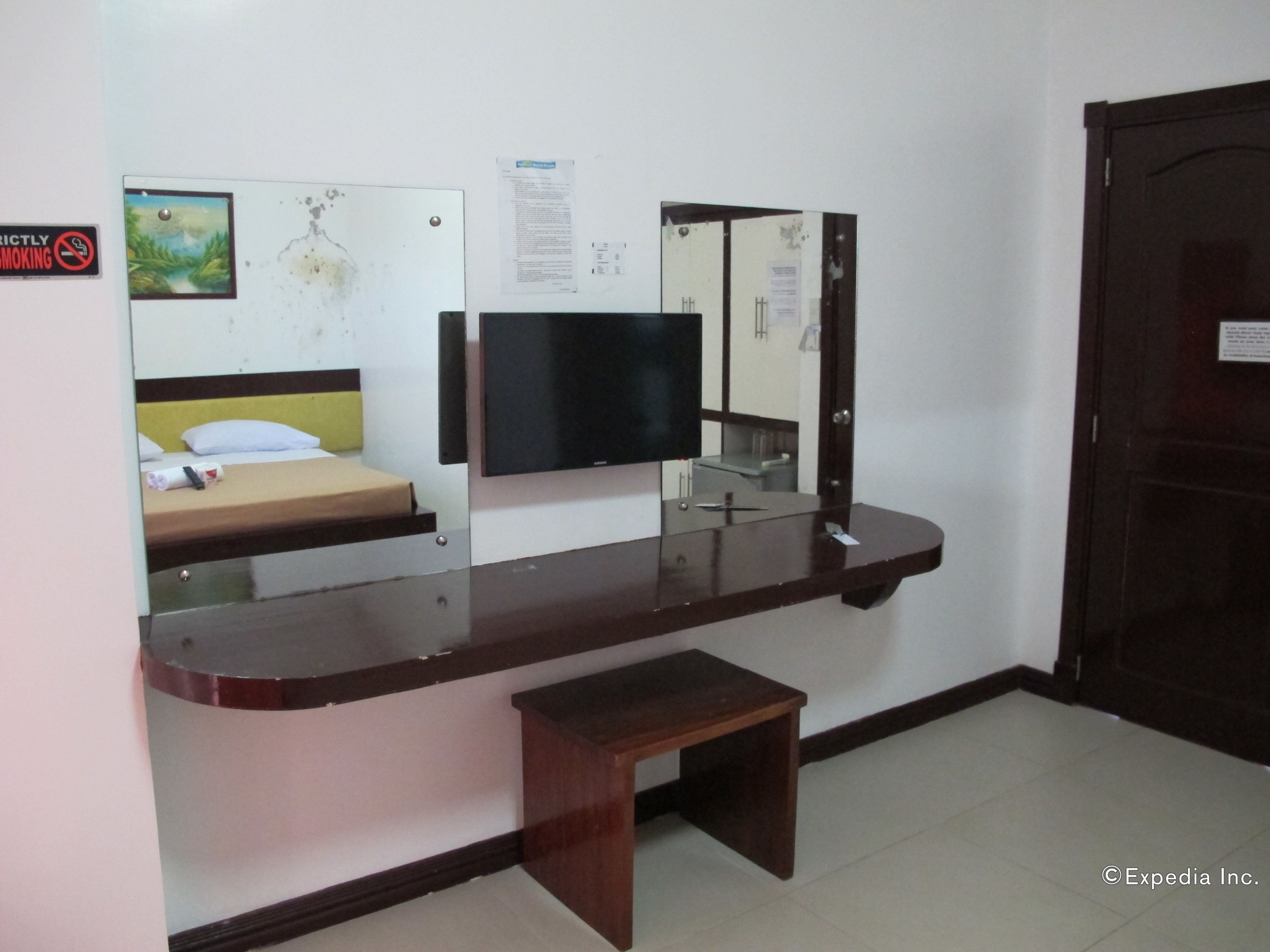 A hotel room with a bed, a desk with a mirror, a television, and a small wooden stool.
