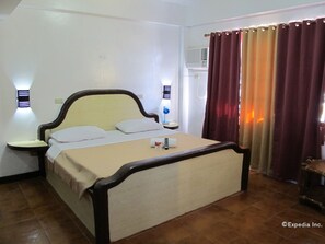 A single bed with a wooden frame and a beige mattress, two bedside tables with lamps, a window with curtains, and an air conditioning unit on the wall. - Seashore Beach Resort (Puerto Galera)