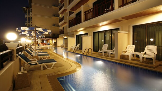 A swimming pool with lounge chairs and umbrellas, surrounded by a building with balconies and large windows. - Jiraporn Hill Resort (Patong)