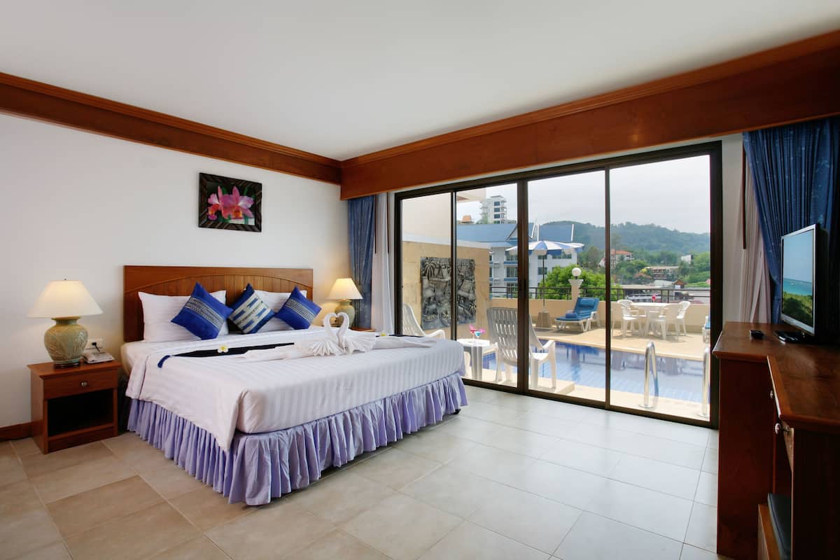 A hotel room with a large bed, a TV, a desk, and a balcony with a pool view.