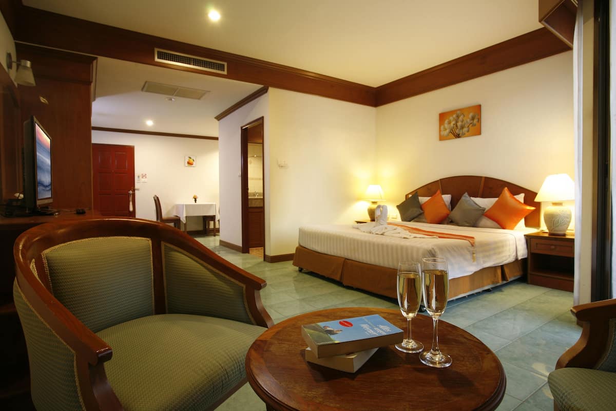A hotel room with a bed, two chairs, a small table with a book and glasses, and a painting on the wall.