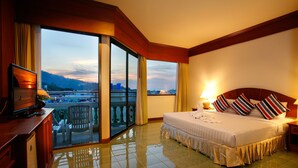 A hotel room with a large bed, a television, a desk with a lamp, and a balcony with a city view. - Jiraporn Hill Resort (Patong)