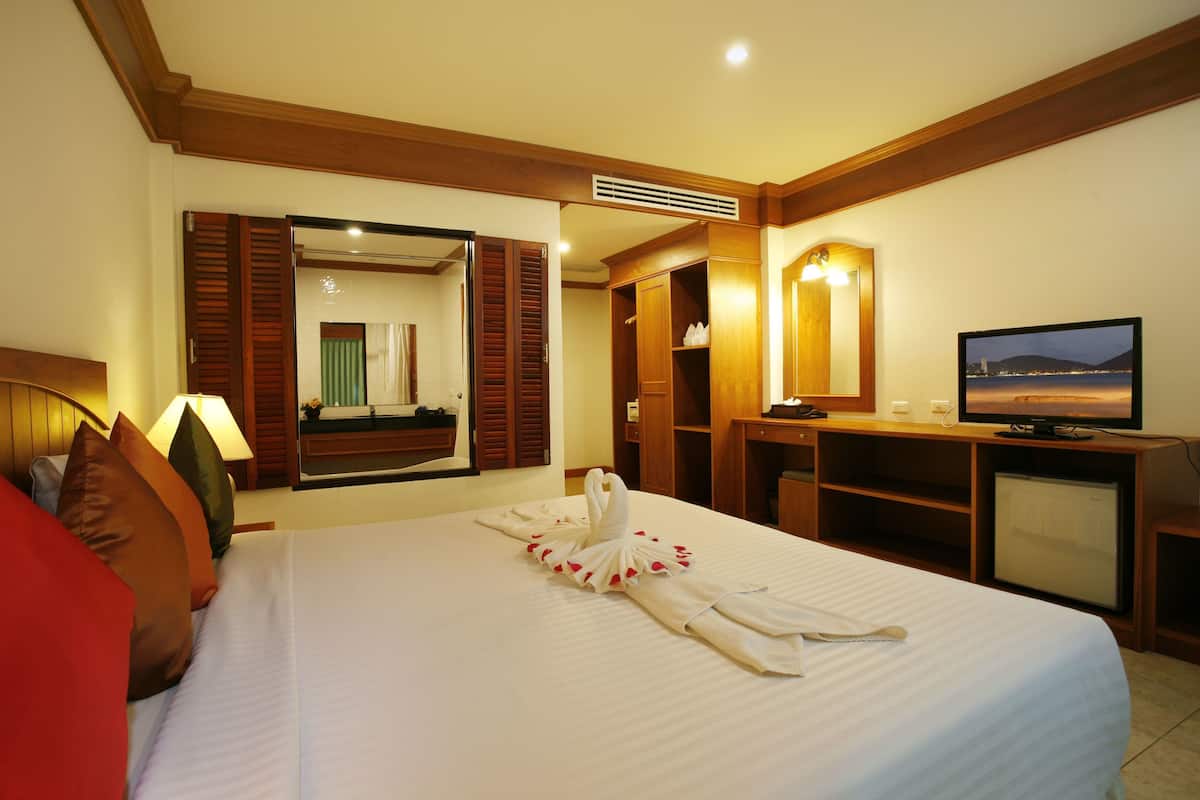 A hotel room with a bed, a TV, a mirror, and a wooden wardrobe.