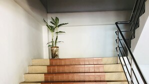 A staircase with alternating beige and brown tiles, a potted plant on the landing, and a metal handrail on the right. - Jiraporn Hill Resort (Patong)