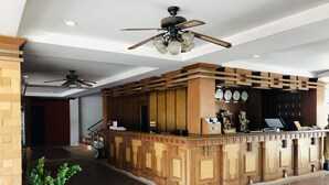 A reception area with a wooden reception desk, ceiling fans, a potted plant, and a tiled floor. - Jiraporn Hill Resort (Patong)