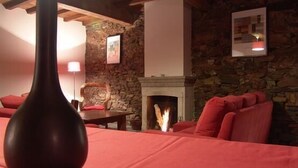 Une pièce chaleureuse avec un mur en pierre, une cheminée, une table à manger agrémentée d’un vase et des meubles rouges.