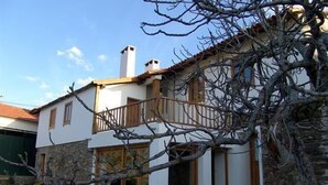 Une maison à deux étages avec une façade en pierre, un balcon en bois et un ciel dégagé.