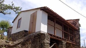 Un bâtiment en pierre avec une façade blanche, des volets en bois et un toit recouvert de tuiles.