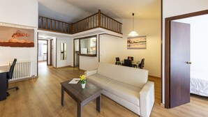 Un amplio salón con techo alto, una escalera de madera, un sofá blanco, una mesa de centro y un comedor con sillas y una mesa.