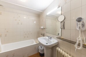 A bathroom with a bathtub, sink, mirror, and hairdryer. - Apartamentos La Solana (Encamp)