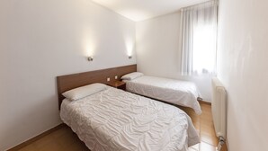 Habitación con dos camas, cabecera de madera, mesita de noche y ventana con cortinas.