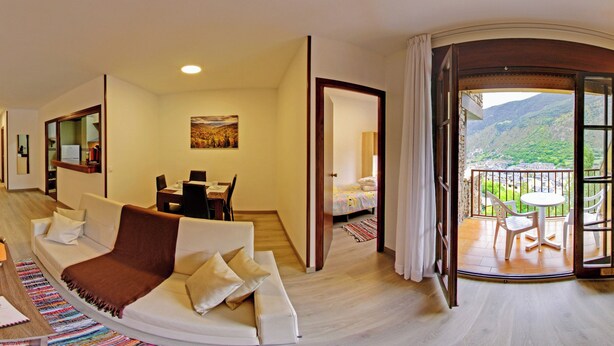 Habitación de hotel con balcón, televisión, sofá y zona de comedor.