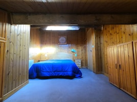 A bedroom with wooden walls, a bed with a blue blanket, a nightstand, a dresser, and a wall-mounted lamp.