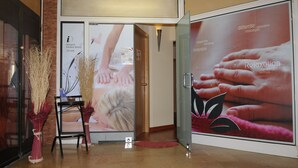 Un espace d’accueil doté d’une porte en verre, d’un comptoir de réception en bois et d’une affiche faisant la promotion de massages et de soins de relaxation.