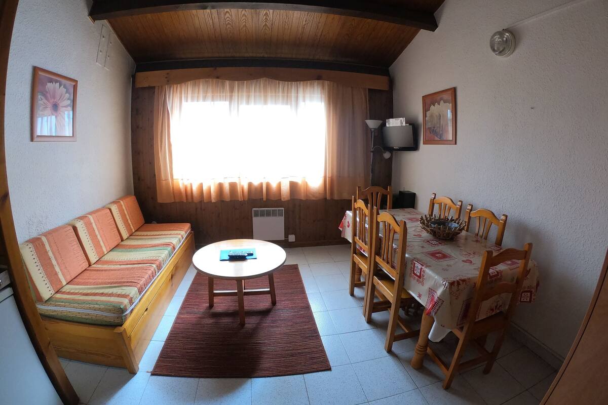 Una sala de estar acogedora con un sofá, una mesa de comedor con sillas y un amplio ventanal con cortinas.