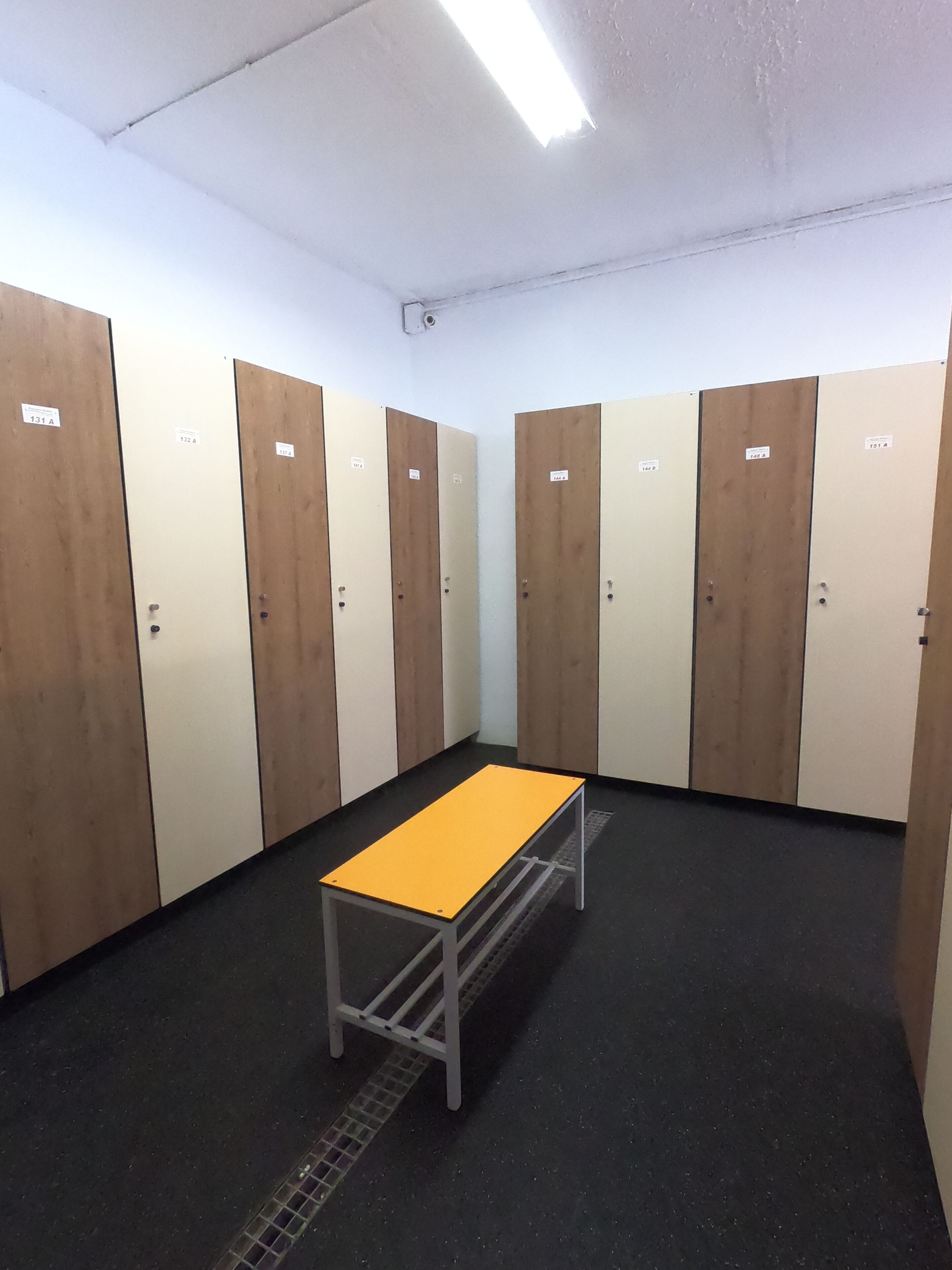 A room with six lockers, a central table, and a drain in the floor.