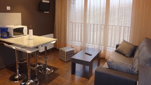 Un espace de vie compact comprenant un coin cuisine, un canapé, une table basse et un téléviseur fixé au mur.