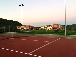 Ein Tennisplatz mit Netz, umgeben von Häusern und einem Berg im Hintergrund.