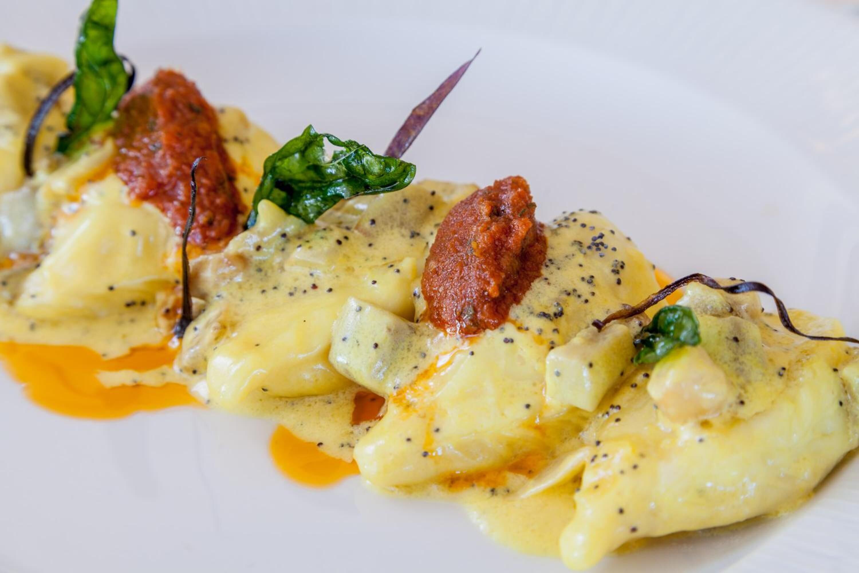 Un plat de raviolis nappés d’une sauce crémeuse, garni de basilic et d’une sauce rouge.