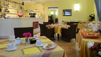 Un espace repas avec des tables préparées pour le petit-déjeuner, où l’on trouve des croissants et du café.