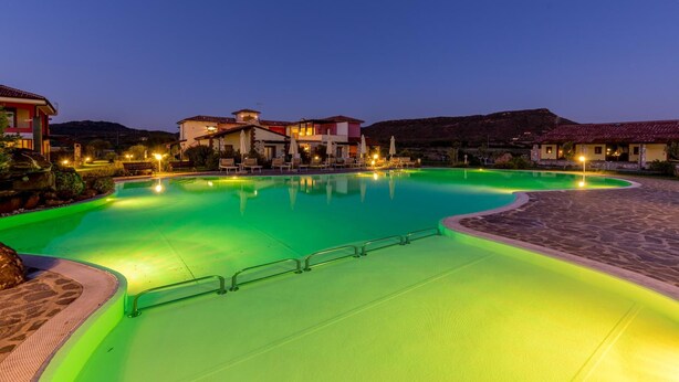 A swimming pool area with a curved design, surrounded by buildings with red-tiled roofs, and a clear view of the surrounding landscape.