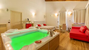 A room with a massage table, a bed, a red sofa, and a small dining area.