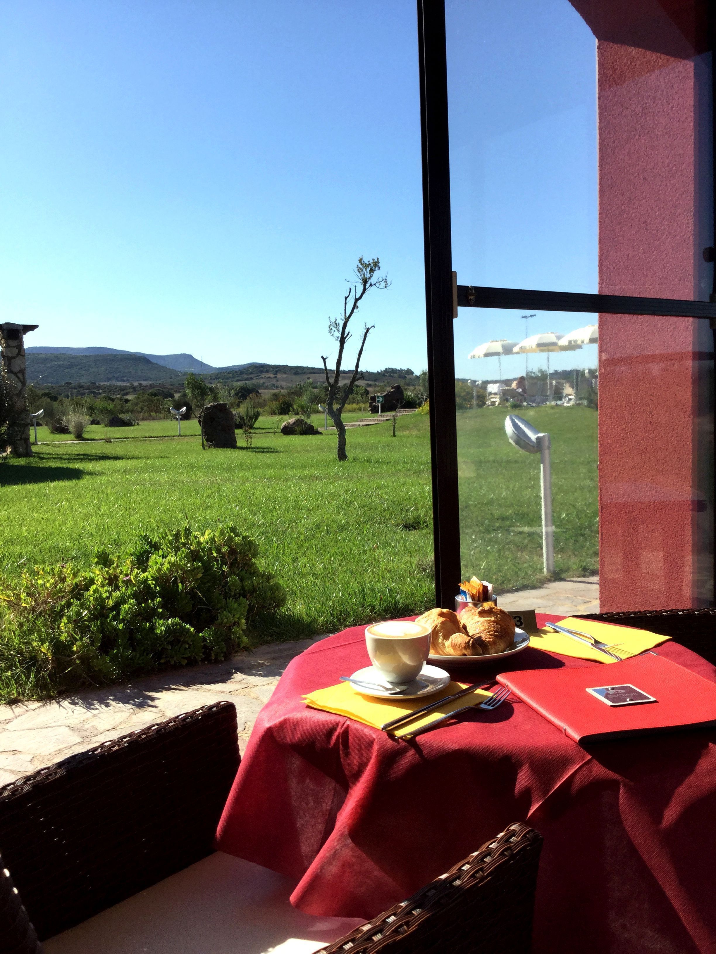 A table with a red tablecloth, a cup of coffee, croissants, and a plate of food.