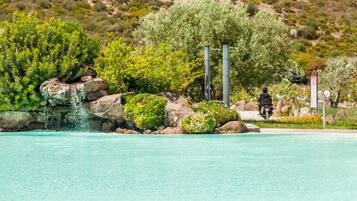 Una piscina con acqua cristallina, circondata da vegetazione e rocce.