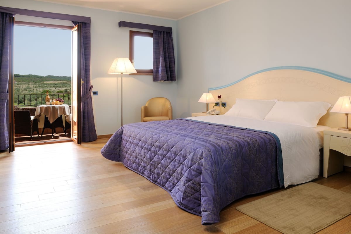 A bedroom with a bed, bedside tables, a chair, a table with a view, and a window.