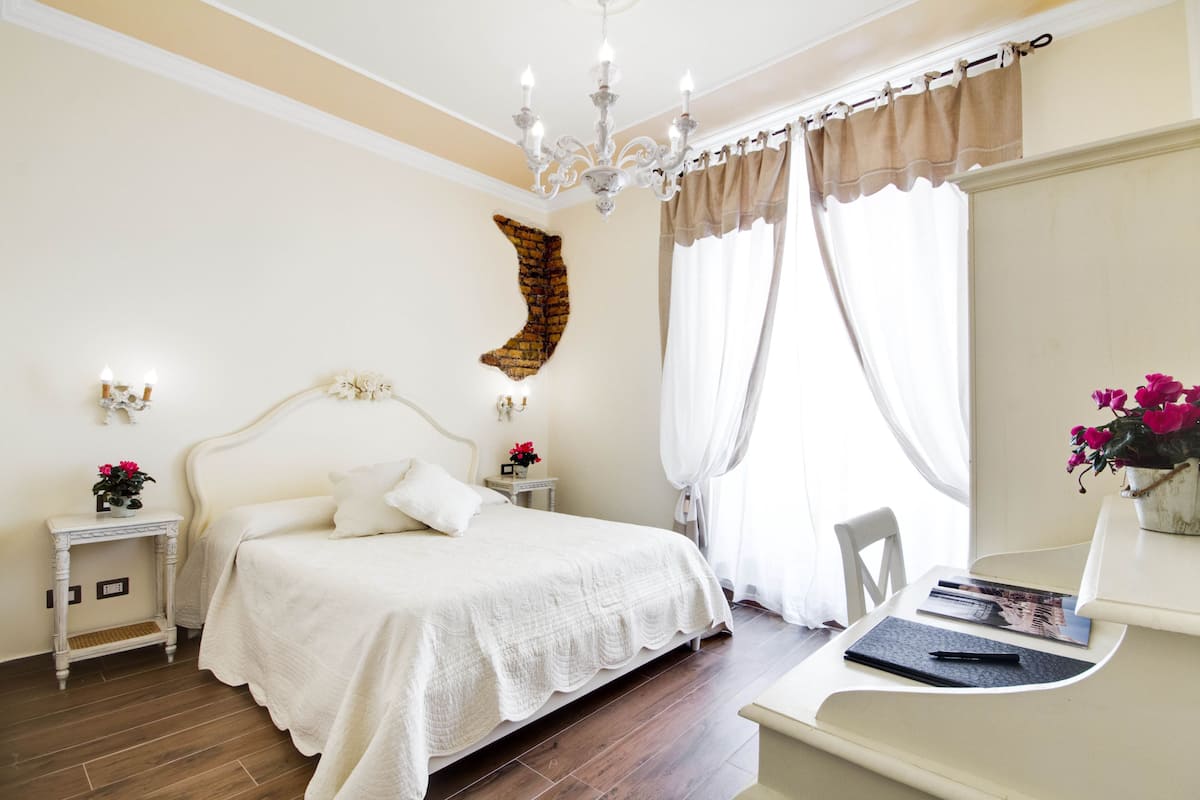 Una camera da letto con un letto grande, comodini, una scrivania con una sedia, un lampadario e una finestra con tende.