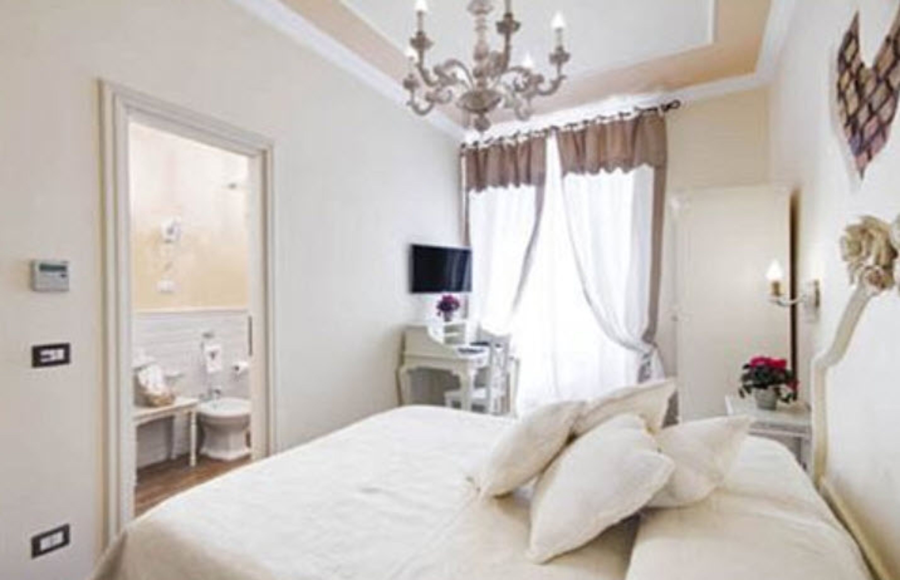 A hotel room with a large bed, a desk, a chair, a television, and a chandelier.