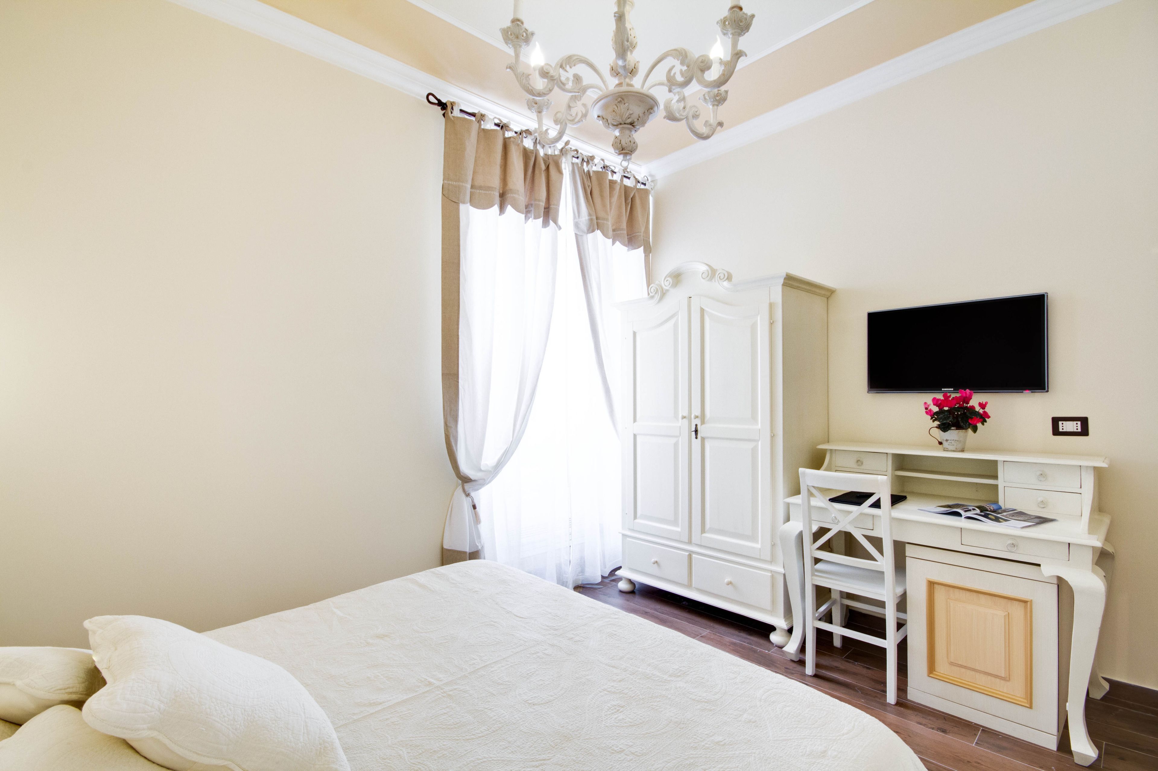 A bedroom with a bed, a desk, a chair, a TV, and a window with curtains.