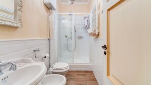 A bathroom with a white sink, a toilet, a glass-enclosed shower, and a wooden floor. - Lunaria Suites Rome (Rome)