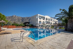 Una piscina con sillones reclinables y un edificio con varios balcones al fondo.