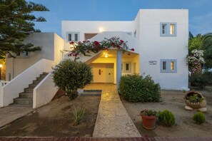 Un edificio moderno con fachada blanca, una escalera que conduce a la entrada y un jardín cuidado con plantas en macetas.