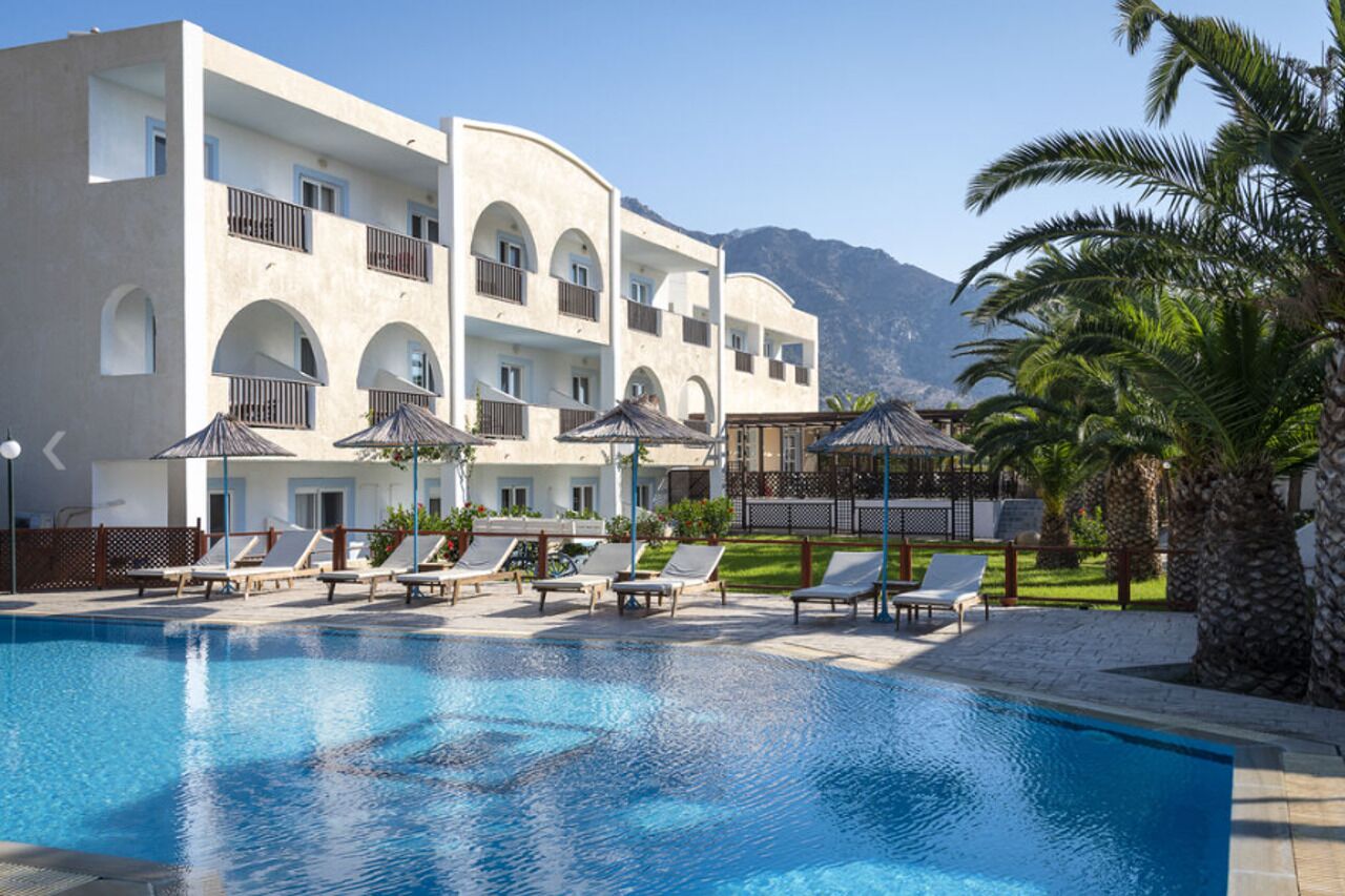 A hotel with a swimming pool, sun loungers, and a view of mountains.
