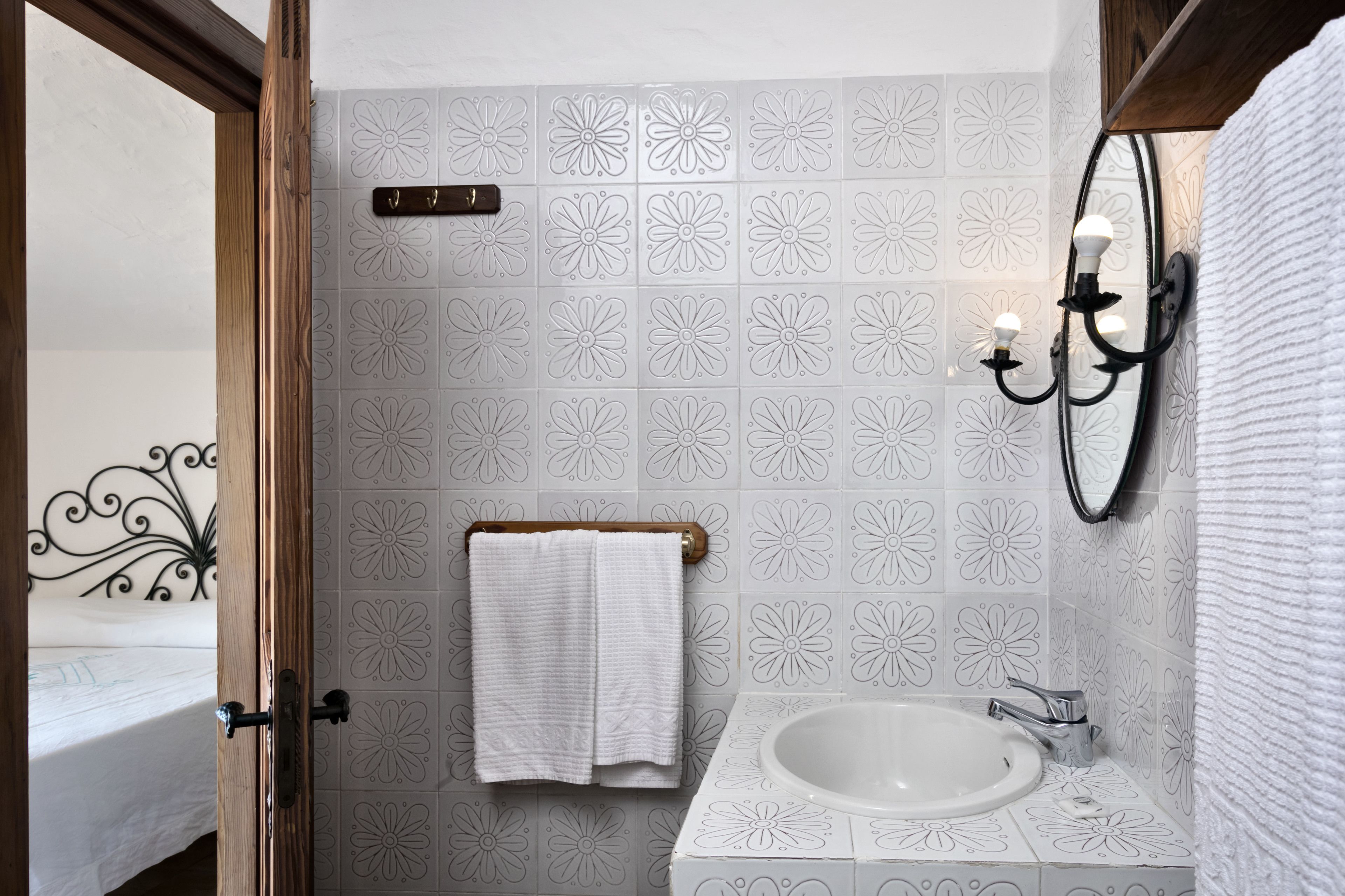 Un baño con un lavamanos blanco, un perchero con una toalla blanca, un espejo y una pared con estampado floral.