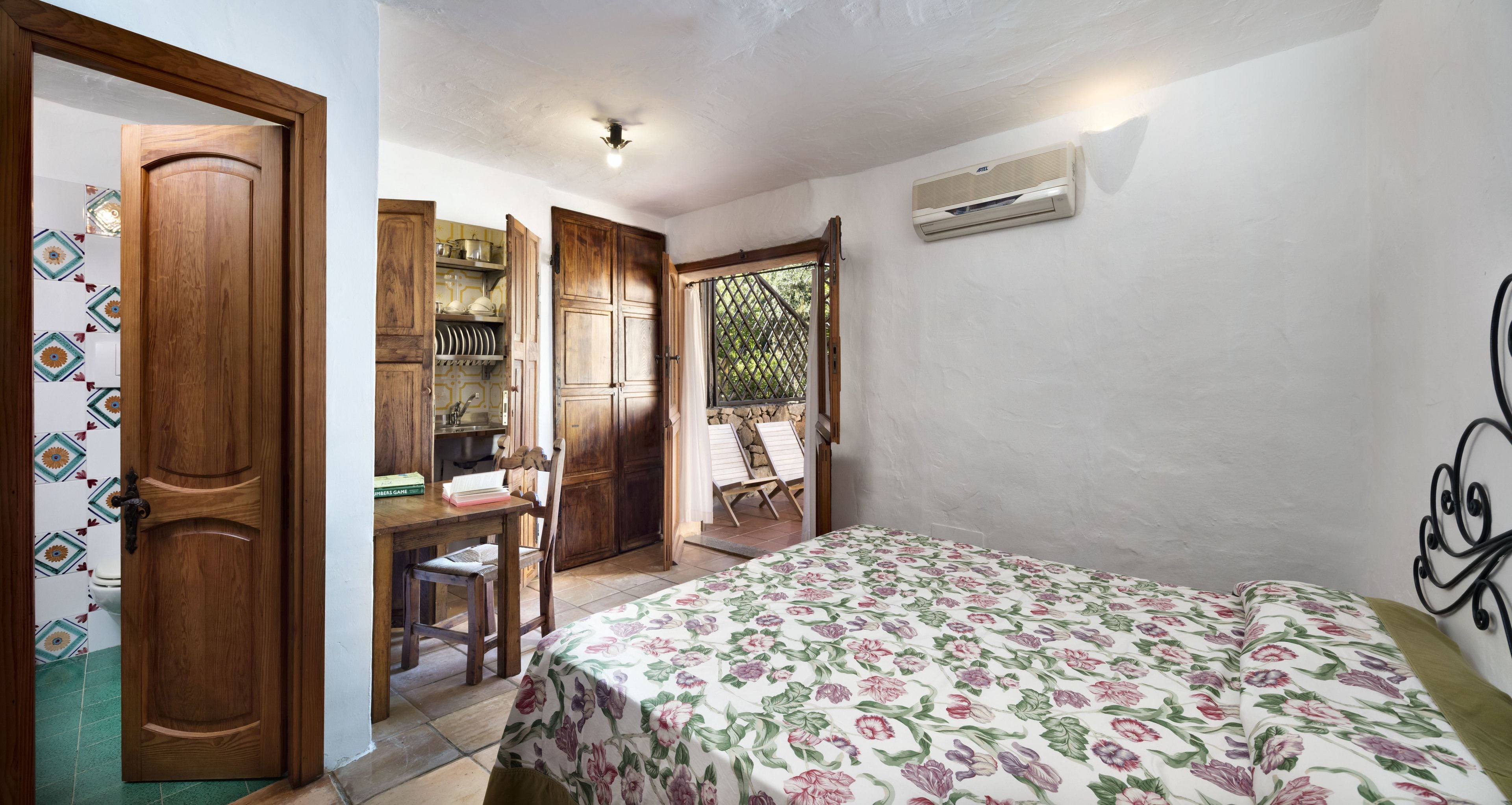 Un dormitorio con cama, un armario de madera, un escritorio con sillas y una pequeña cocina.