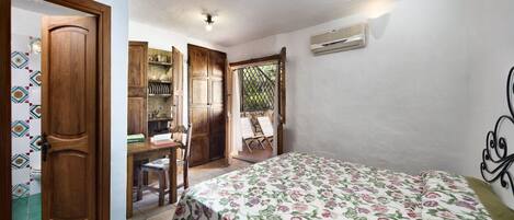 Un dormitorio con cama, un armario de madera, un escritorio con sillas y una pequeña cocina.