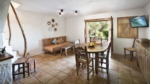 A dining area with a wooden table and chairs, a sofa, and a television mounted on the wall. - Residenza Capriccioli (Arzachena)