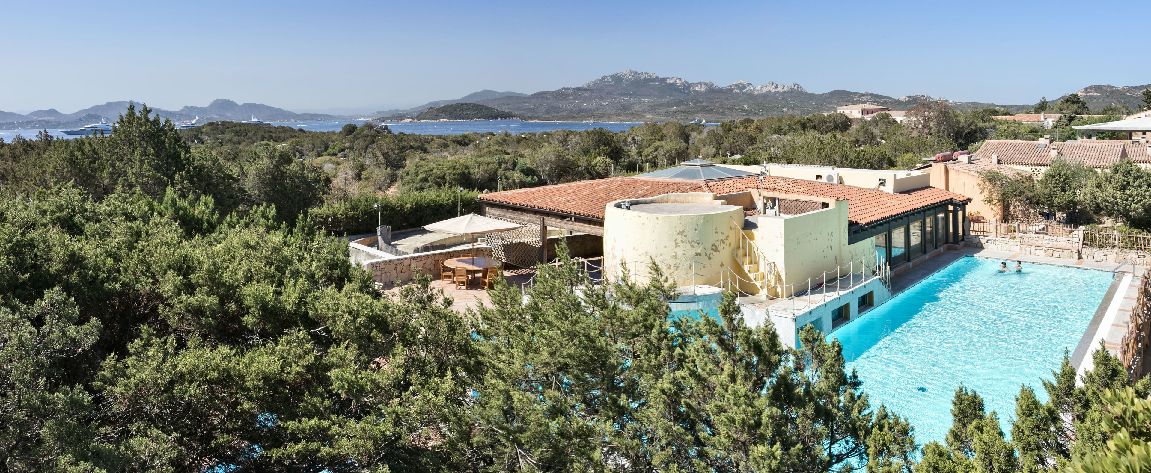 Un complexe hôtelier doté d’une piscine, d’un espace extérieur couvert avec des sièges, et offrant une vue sur la mer et les montagnes.