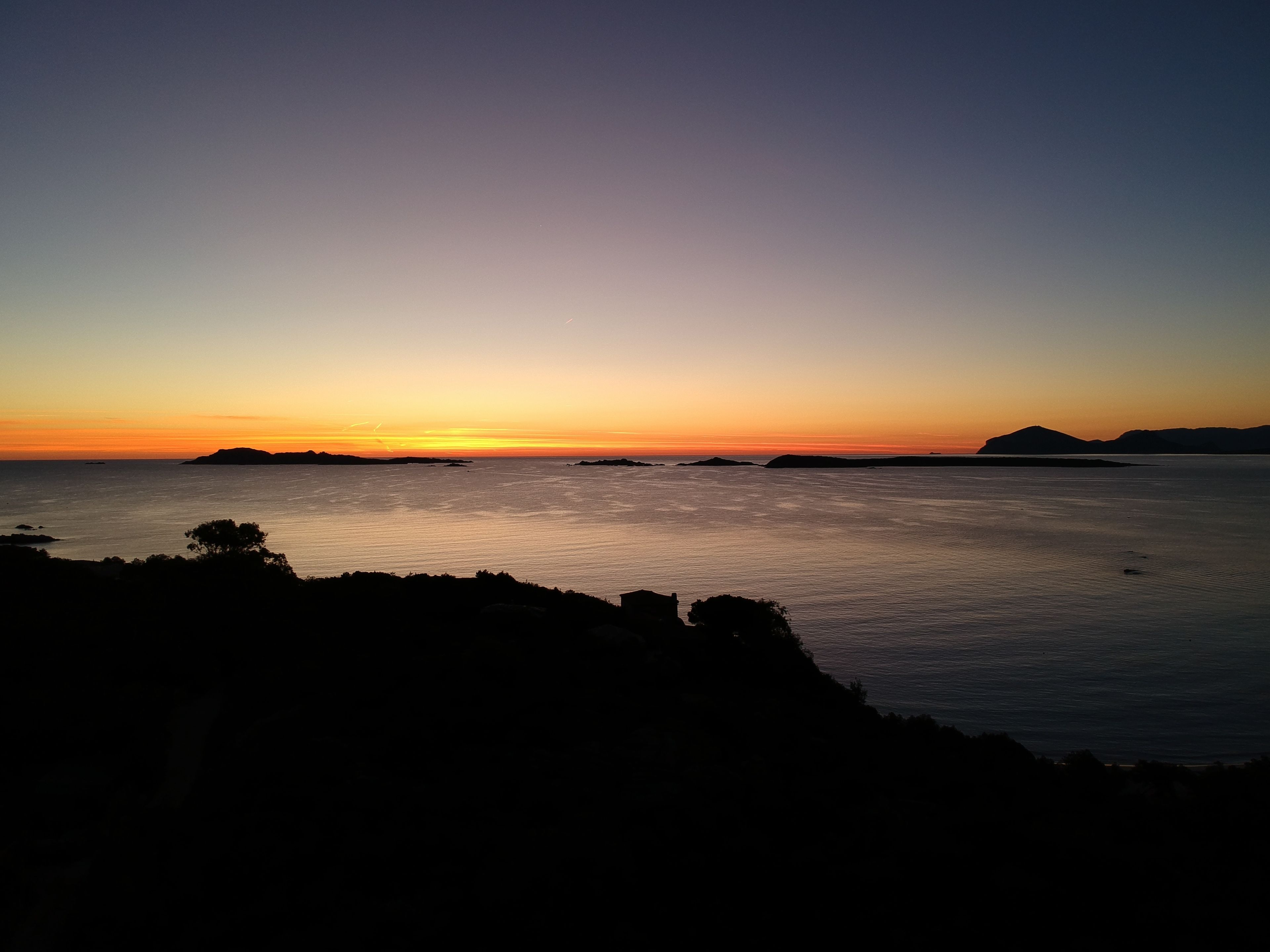 A coastal sunset view with calm waters and distant landforms.