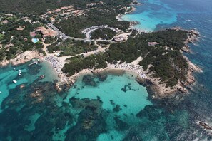An aerial view of a coastal area with a beach, parking lot, and buildings. - Residenza Capriccioli (Arzachena)