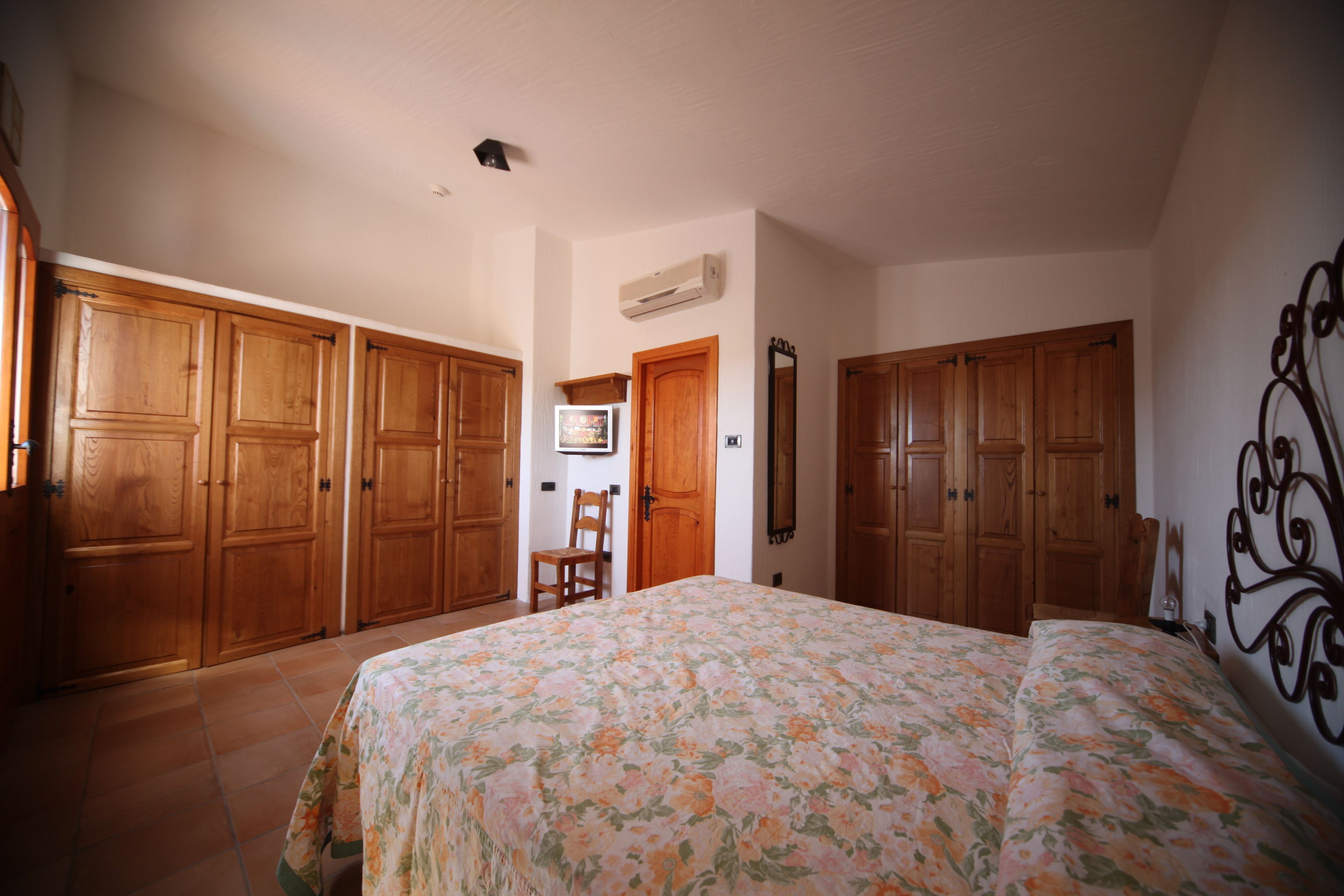 A bedroom with a large bed, wooden wardrobes, a chair, and a mirror.