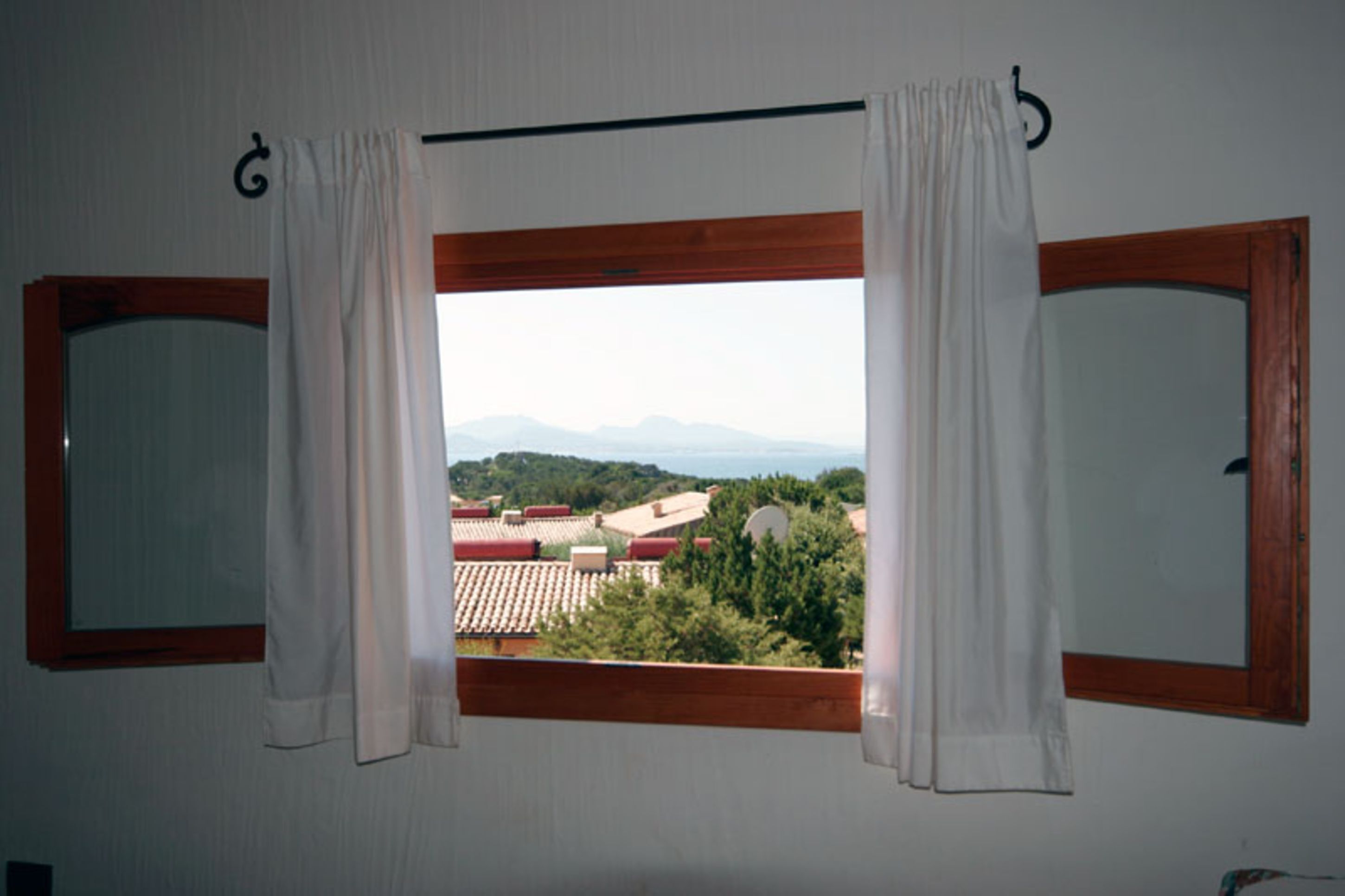 A room with a window overlooking a landscape with buildings and mountains.