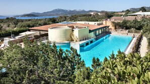 A swimming pool with a clear view of the surrounding landscape, including trees and distant mountains. - Residenza Capriccioli (Arzachena)