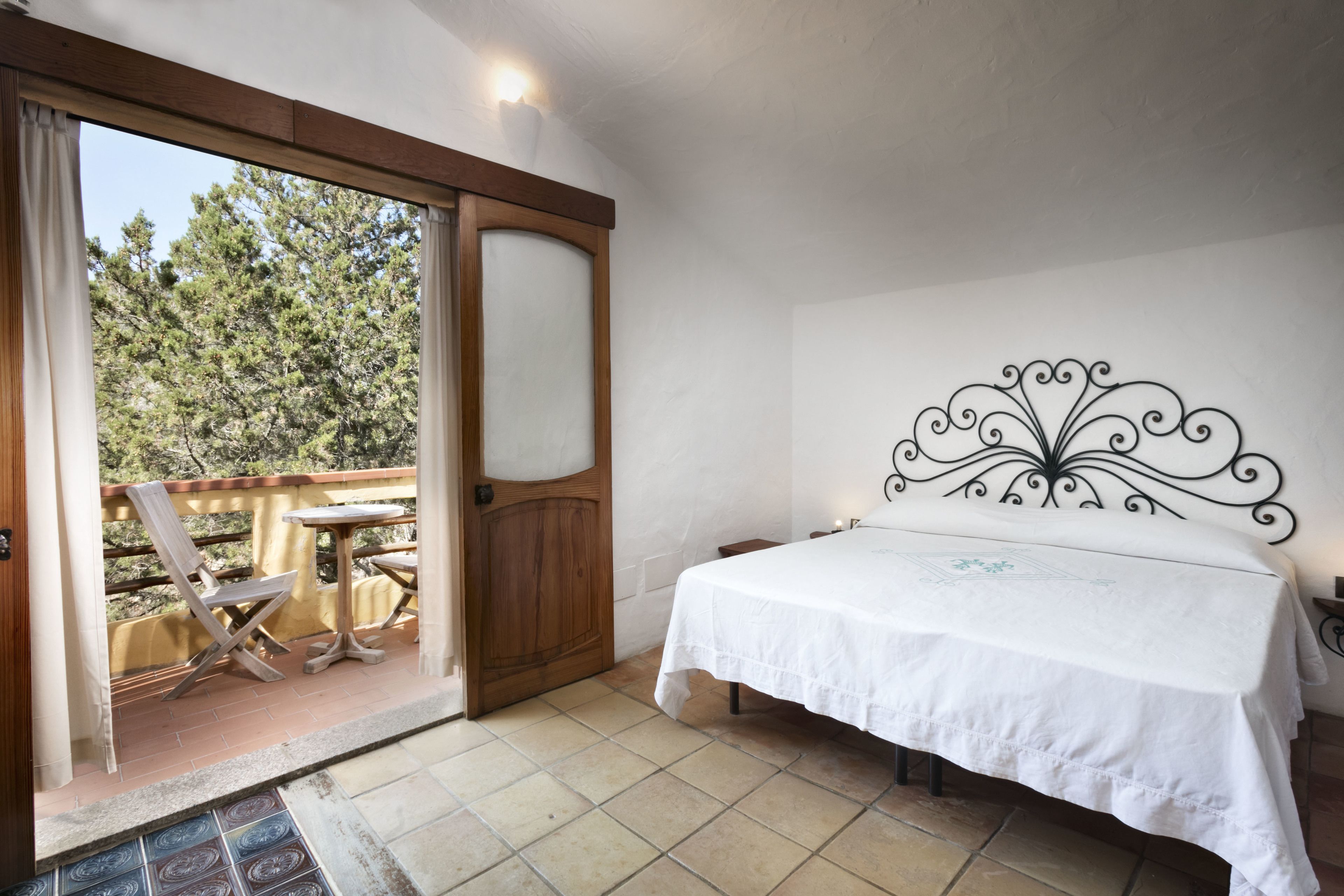 Ein Schlafzimmer mit einem Bett, einer Holztür, die zu einem Balkon führt, und einem Metall-Kopfteil.