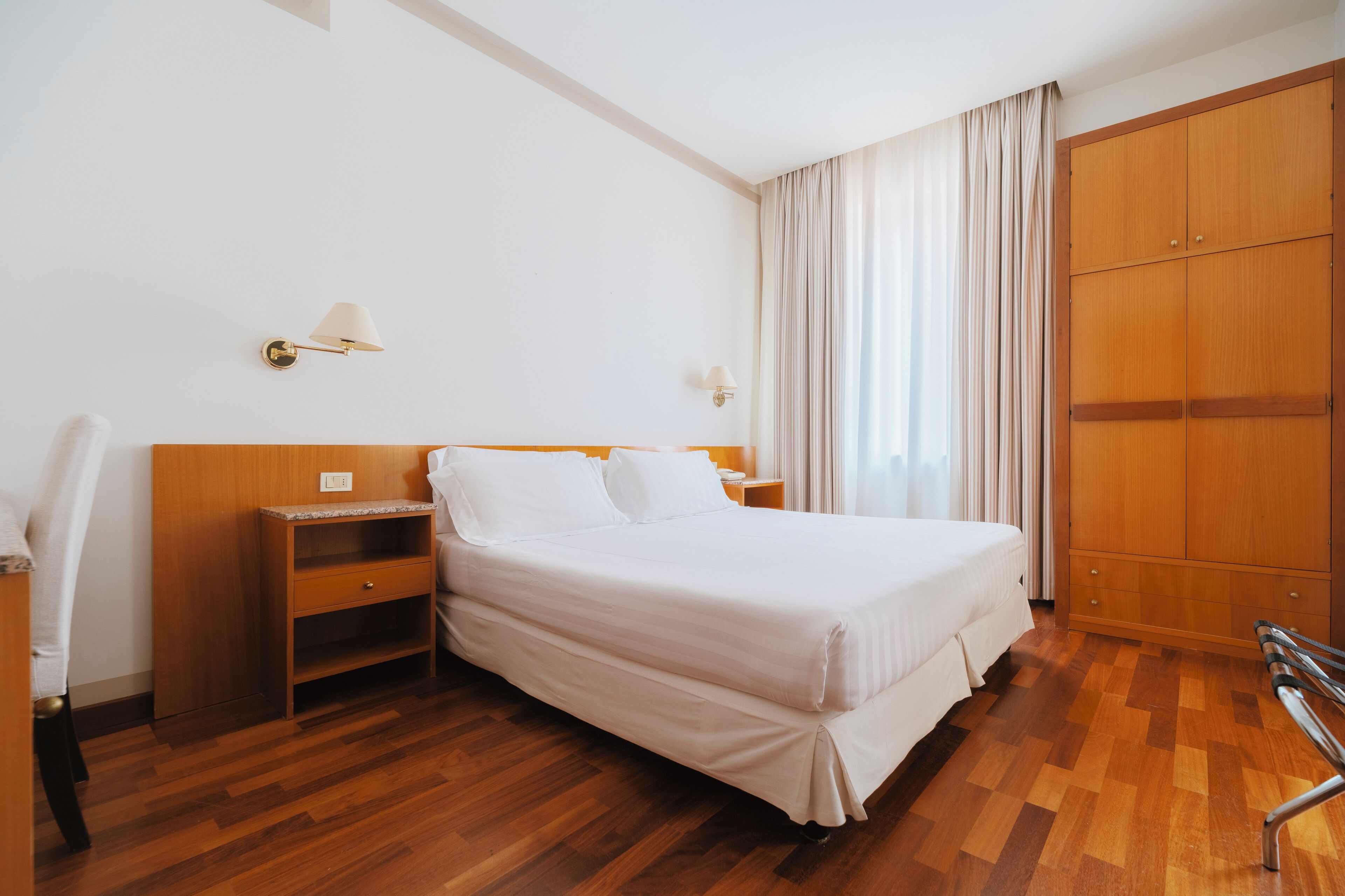 Una habitación de hotel con una cama grande, un armario de madera, mesitas de noche y una lámpara.